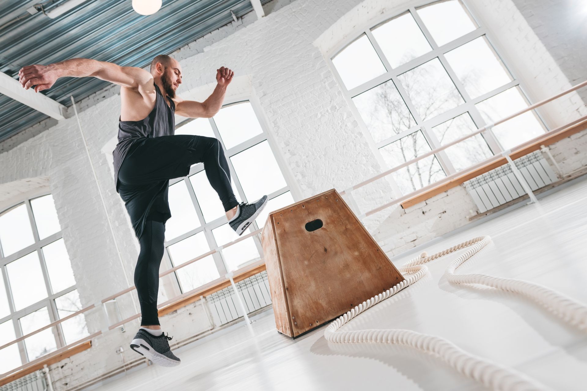 Strong fitness man doing jump exercises on box in gym. Fit athlete wearing sportswear and jumping over box in sport hall